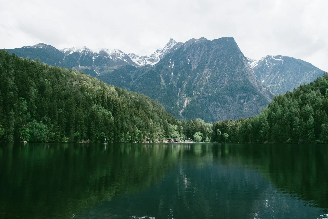 A forest-lined lake beneath dramatic alpine peaks